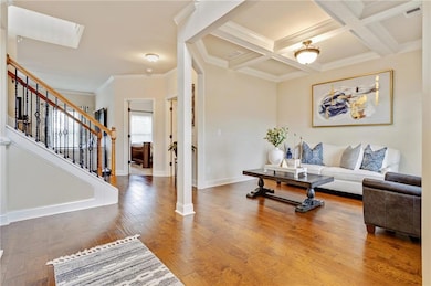 Living area featuring coffered ceiling, beam ceiling, crown molding, wood finished floors, and stairs