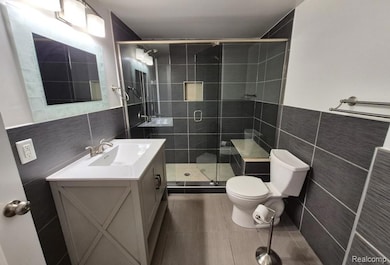 Full bathroom featuring tile walls, vanity, a shower stall, and dark tile patterned floors