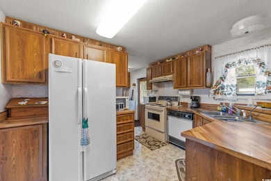 Kitchen with white appliances, brown cabinetry, wallpapered walls, a textured ceiling, and butcher block countertops