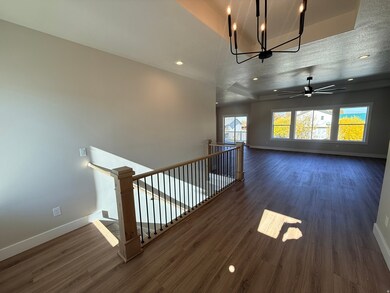Unfurnished living room featuring dark wood-style flooring, a chandelier, recessed lighting, a ceiling fan, and a tray ceiling