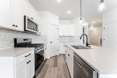 Kitchen with stainless steel appliances, light wood finished floors, a kitchen island with sink, light countertops, and hanging light fixtures