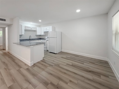 This photo showcases a modern, open-concept kitchen with light wood flooring, white cabinetry, and granite countertops. The space includes a large island with seating, ample natural light, and recessed lighting for a bright, inviting atmosphere.