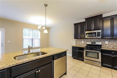 Kitchen with stainless steel appliances, pendant lighting, light stone countertops, and light tile patterned floors