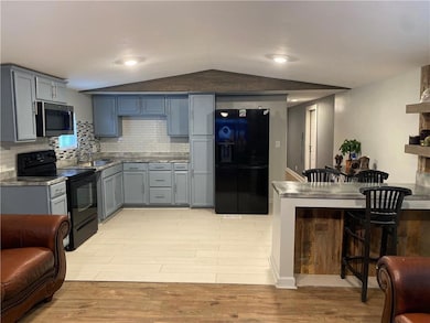 Kitchen featuring black appliances, decorative backsplash, gray cabinetry, light wood-style floors, and vaulted ceiling