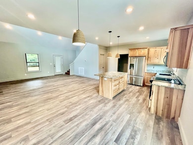Kitchen featuring a kitchen island, stainless steel fridge, light wood finished floors, hanging light fixtures, and recessed lighting