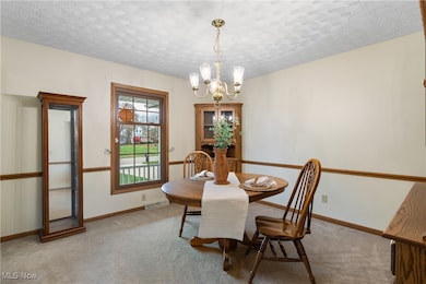 Carpeted dining room featuring a textured ceiling and a chandelier