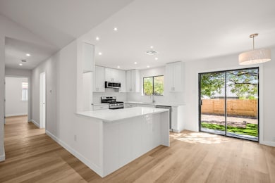 Kitchen featuring white cabinetry, light wood-type flooring, appliances with stainless steel finishes, decorative light fixtures, and light stone counters