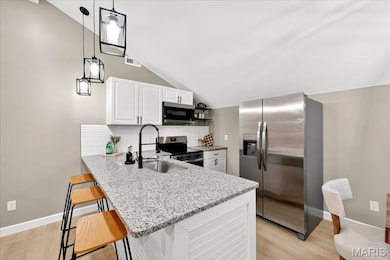 Kitchen featuring stainless steel appliances, vaulted ceiling, decorative backsplash, light wood-style flooring, and light stone counters