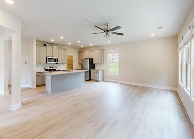 Kitchen with light hardwood / wood-style floors, a center island with sink, stainless steel appliances, and gray cabinetry