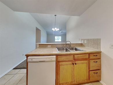 Kitchen with white dishwasher, a sink, a peninsula, pendant lighting, and a chandelier
