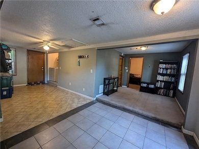 Unfurnished living room with a textured ceiling, light tile patterned floors, a ceiling fan, and light colored carpet
