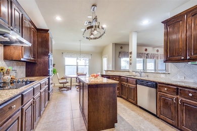 Kitchen with decorative backsplash, stainless steel appliances, a center island, light stone countertops, and pendant lighting