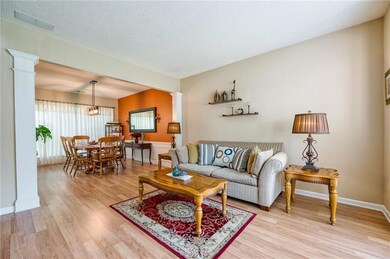 Living area with decorative columns, light wood finished floors, a chandelier, a textured ceiling, and baseboards