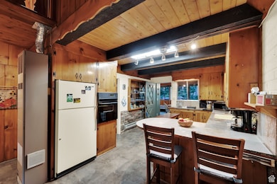 Kitchen featuring freestanding refrigerator, a peninsula, oven, a kitchen breakfast bar, and a wooden ceiling with exposed beams