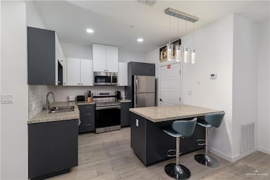 Kitchen with decorative backsplash, visible vents, appliances with stainless steel finishes, light wood-type flooring, and a sink