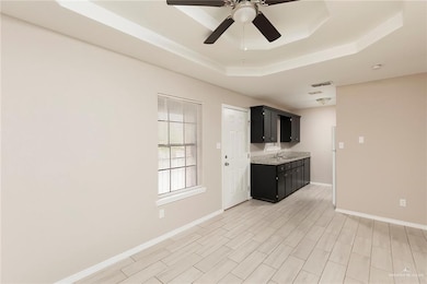 Kitchen featuring a sink, a ceiling fan, a raised ceiling, baseboards, and dark cabinets