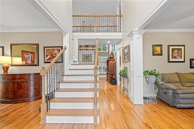 Staircase with ornate columns, crown molding, wood finished floors, and a high ceiling