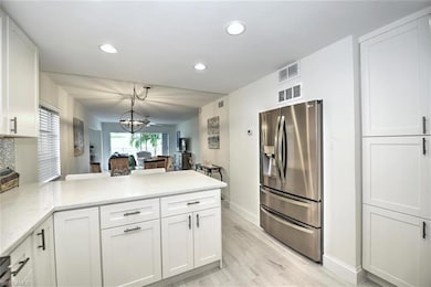 Kitchen with stainless steel fridge, a peninsula, white cabinets, and recessed lighting