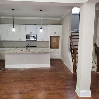 Kitchen with stainless steel microwave, a sink, ornamental molding, an island with sink, and white cabinets