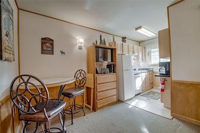 Kitchen featuring light brown cabinets, wooden walls, light tile patterned floors, and white appliances