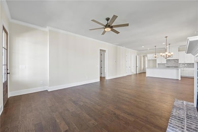Unfurnished living room with crown molding, dark wood-type flooring, a chandelier, and a ceiling fan