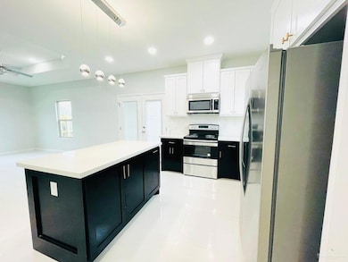 Kitchen featuring appliances with stainless steel finishes, dark cabinets, white cabinets, decorative light fixtures, and light tile patterned floors
