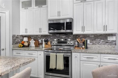 Kitchen with stainless steel appliances, white cabinets, and light stone countertops