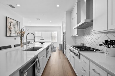 Kitchen with white cabinetry, stainless steel appliances, wall chimney range hood, recessed lighting, and dark wood-style floors