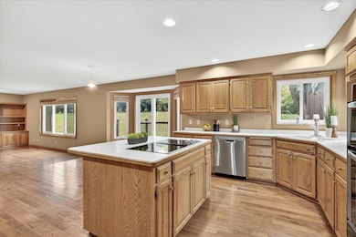 Expansive kitchen with a center island cooktop, stainless steel appliances, double wall ovens, and ample oak cabinetry. Features hardwood floors, recessed lighting, and a bright bayed dining nook with access to the backyard deck.