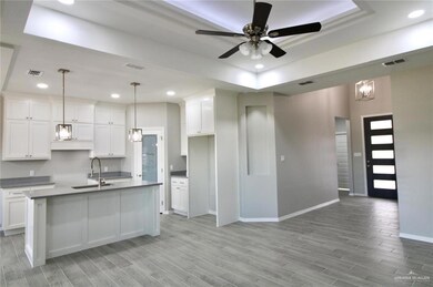 Kitchen featuring a tray ceiling, ceiling fan with notable chandelier, hanging light fixtures, sink, and white cabinets