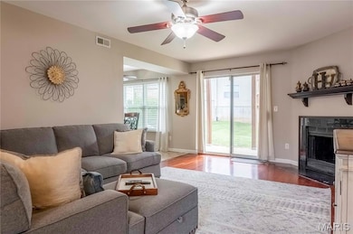 Living area featuring wood finished floors, plenty of natural light, a fireplace with flush hearth, and ceiling fan
