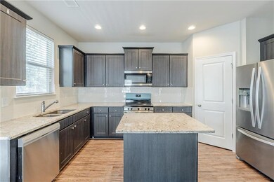 Kitchen featuring a sink, a kitchen island, tasteful backsplash, appliances with stainless steel finishes, and light wood-style floors