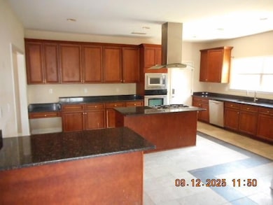 Kitchen featuring brown cabinetry, island exhaust hood, appliances with stainless steel finishes, dark stone countertops, and a center island