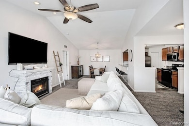 Living room with carpet floors, a fireplace, lofted ceiling, and a ceiling fan