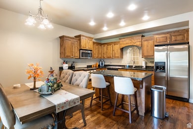 Kitchen featuring appliances with stainless steel finishes, dark wood finished floors, a center island, brown cabinetry, and a chandelier