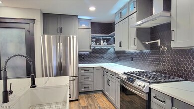 Kitchen featuring light stone countertops, backsplash, light hardwood / wood-style flooring, wall chimney range hood, and stainless steel appliances