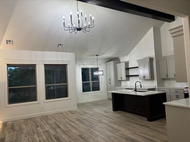 Kitchen featuring a chandelier, high vaulted ceiling, wood finished floors, backsplash, and a kitchen island with sink