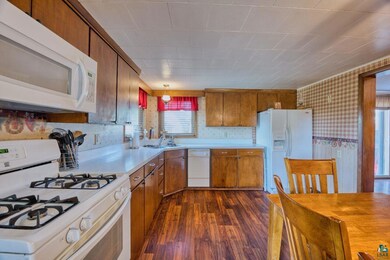 Kitchen with white appliances, light countertops, wallpapered walls, dark wood-style flooring, and brown cabinetry