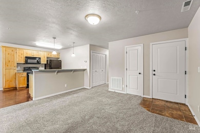 Kitchen featuring black appliances, dark carpet, a textured ceiling, a peninsula, and pendant lighting