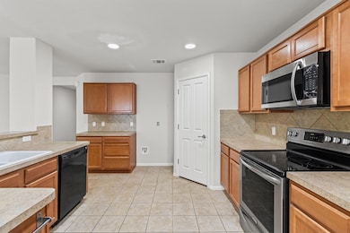 Kitchen with stainless steel appliances, light countertops, tasteful backsplash, light tile patterned floors, and brown cabinets