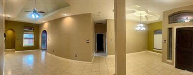Tiled empty room with a raised ceiling, a high ceiling, and ceiling fan with notable chandelier