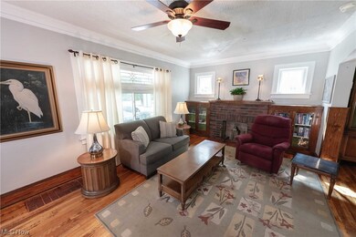 Living room featuring plenty of natural light,  crown molding, hardwood floors, charming built in cabinetry, and ceiling fan.