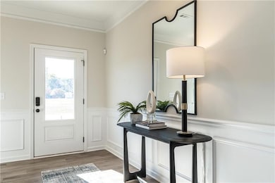 Entryway featuring crown molding, wainscoting, wood finished floors, and a decorative wall