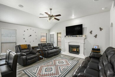 Living room with vaulted ceiling, a warm lit fireplace, wood finished floors, and a ceiling fan