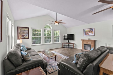 Living room featuring a ceiling fan, wood finished floors, lofted ceiling, and fireplace,