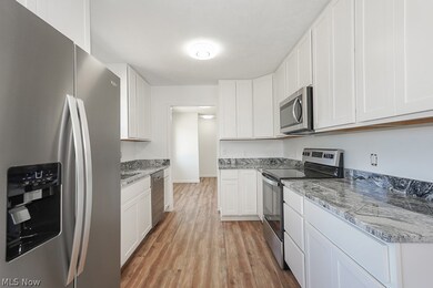 Kitchen featuring white cabinets, light hardwood / wood-style flooring, stainless steel appliances, and light stone counters