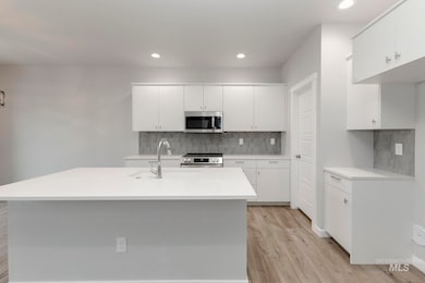 Kitchen with white cabinetry, backsplash, appliances with stainless steel finishes, light wood-type flooring, and recessed lighting
