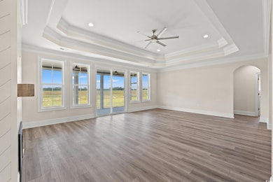 Empty room with a tray ceiling, ceiling fan, arched walkways, crown molding, and wood finished floors