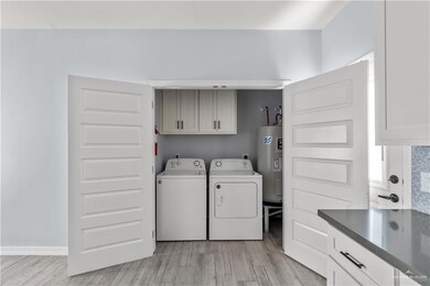 Laundry room with electric water heater, washing machine and clothes dryer, cabinet space, and light wood-style floors