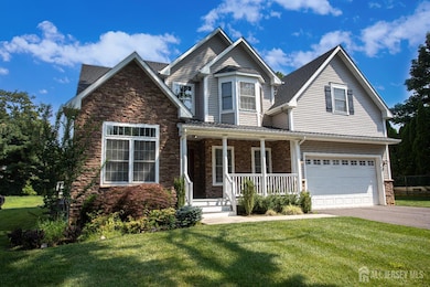 View of front stone facade featuring covered porch, driveway, a front lawn, and a garage
